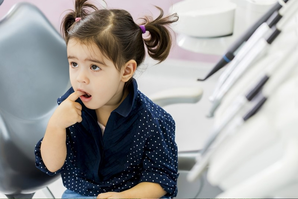 Young girl in dental chair with finger in mouth, appearing nervous during dental visit.