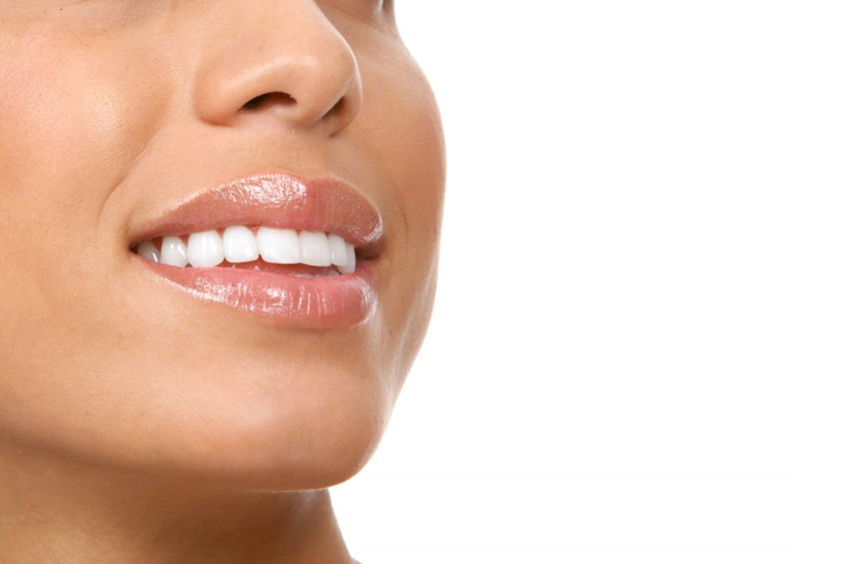 Woman smiling brightly, displaying healthy white teeth and natural complexion against white background.