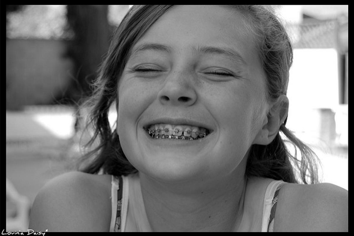 Young girl smiling brightly, displaying healthy teeth and genuine happiness in black and white portrait.