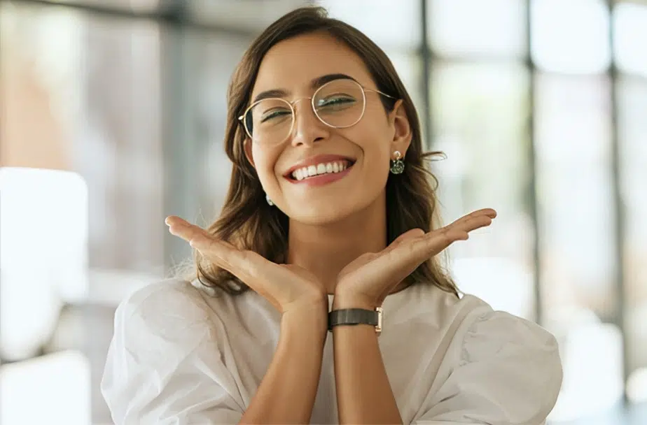 Smiling woman wearing glasses blowing a kiss in a modern dental office setting.