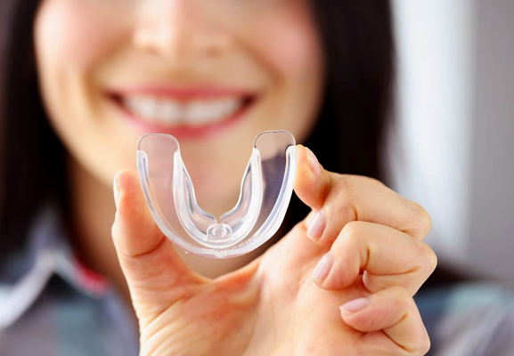 Smiling woman holding clear dental retainer in her hand, promoting orthodontic care.