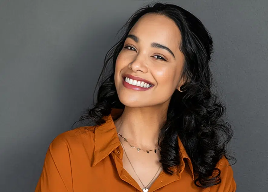 Smiling woman in orange shirt against gray background, dental practice portrait.
