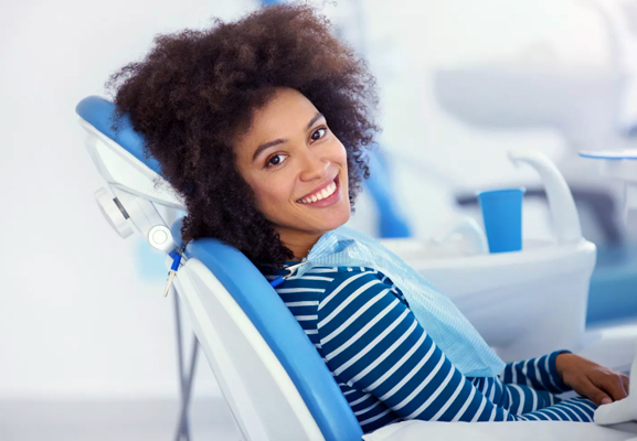 Woman smiling in dental chair wearing blue striped shirt at dentist office