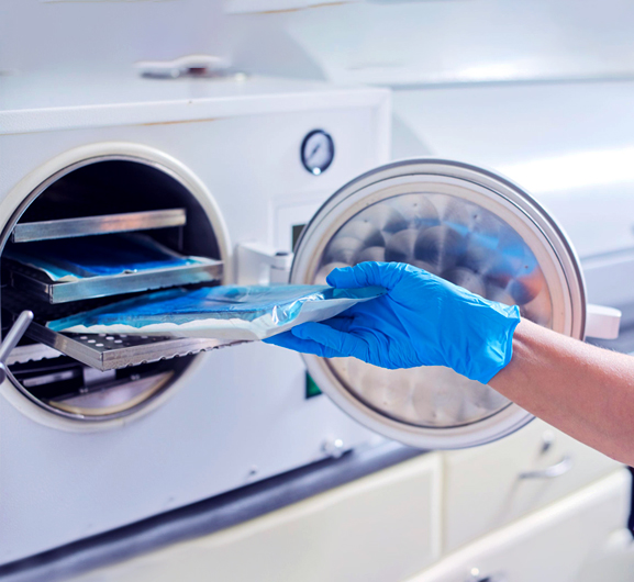 Person placing blue sterilized dental instruments into dental autoclave sterilization machine.