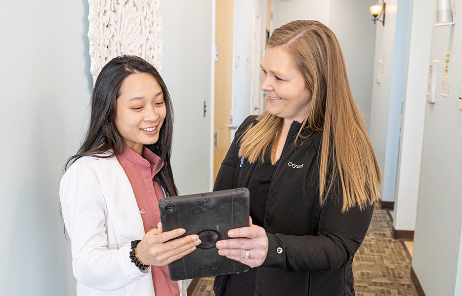 Two women reviewing tablet in dental office hallway setting.