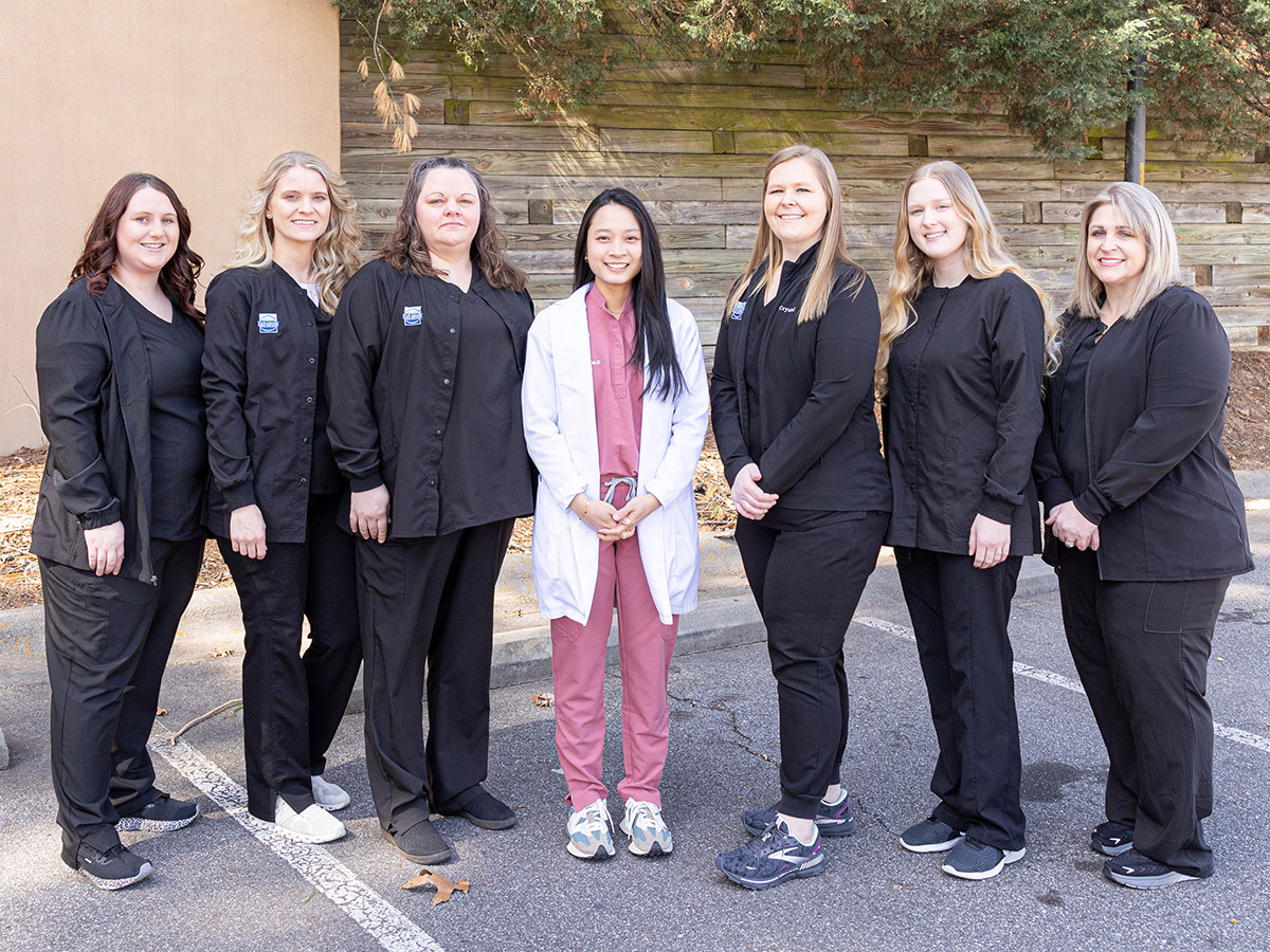 Dental team of eight women in black uniforms standing together outdoors against a building.