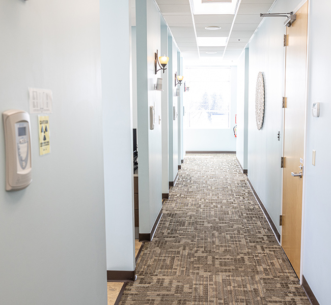 Clean modern dental office hallway with white walls, brown tile flooring, and multiple treatment room doors.