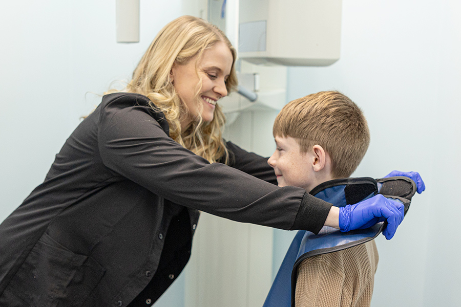 Woman in business attire teaching young boy proper tooth brushing technique in dental office.