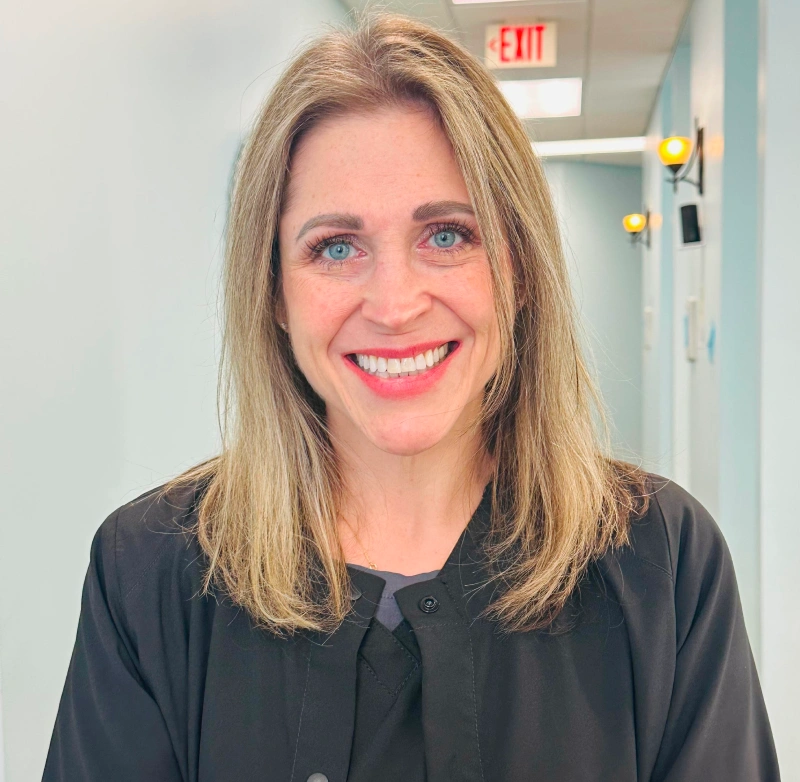 Professional headshot of smiling woman in black shirt in dental office hallway